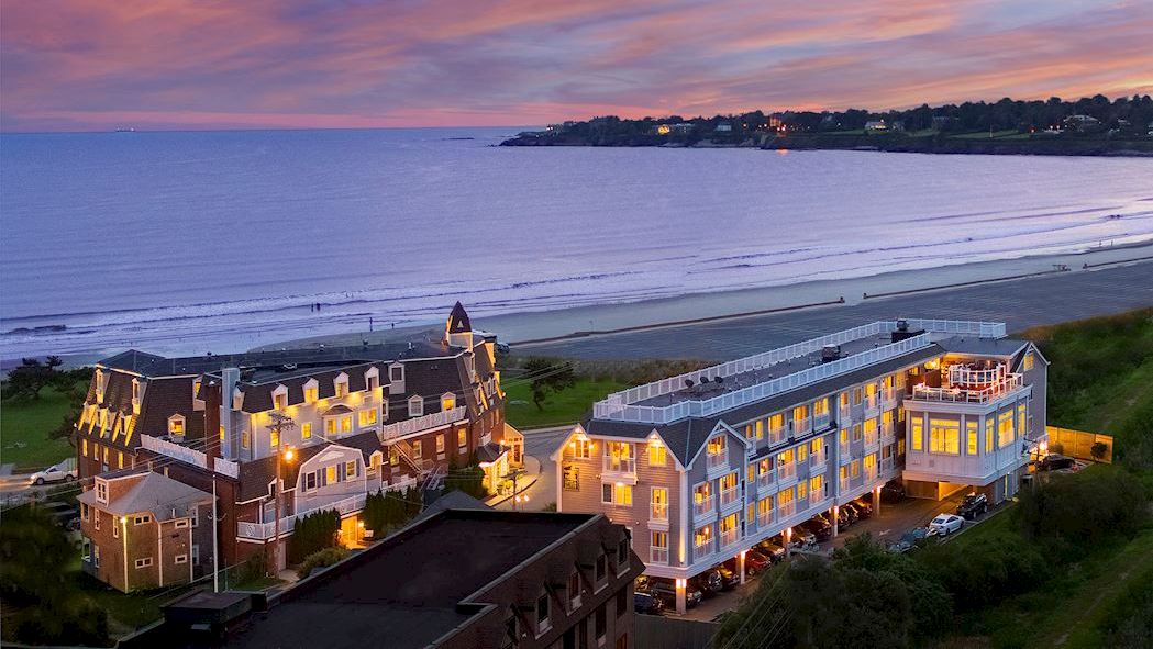 The image depicts a scenic coastline view during sunset with buildings, including a beautiful beachfront hotel or resort.