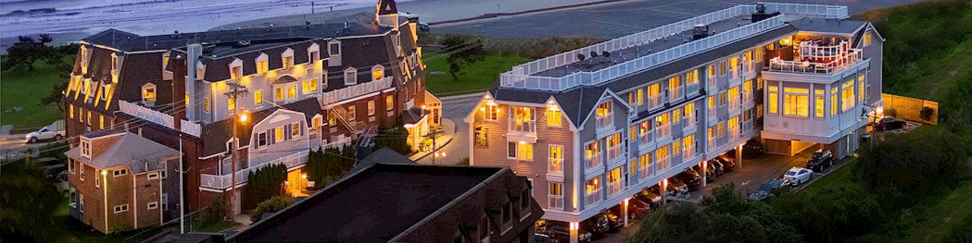 The image depicts a scenic coastline view during sunset with buildings, including a beautiful beachfront hotel or resort.