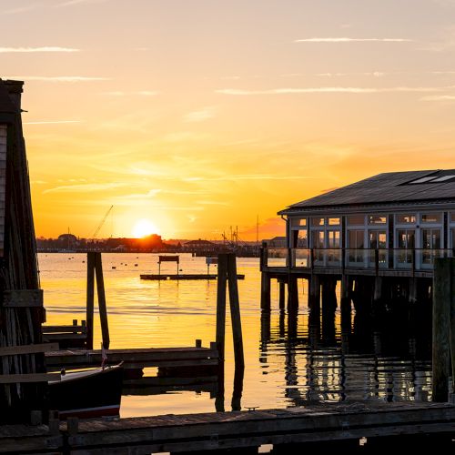 The image shows a serene waterfront with buildings and docks at sunset, with golden hues reflecting on the calm water, ending the sentence.