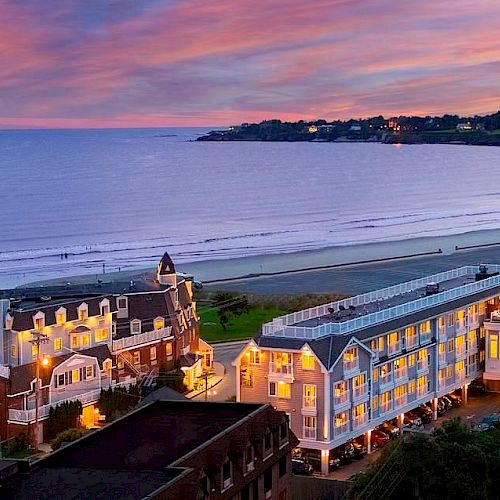 A seaside resort featuring two illuminated buildings with a sandy beach and ocean in the background during sunset.