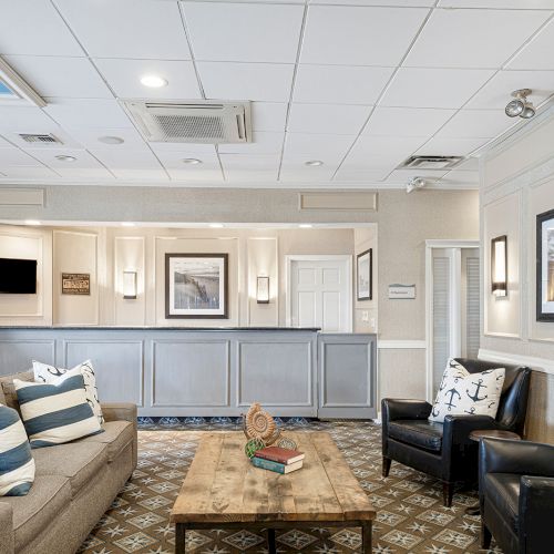 The image shows a nicely decorated waiting area or lobby with comfortable seating, nautical-themed pillows, and framed photographs on the walls.