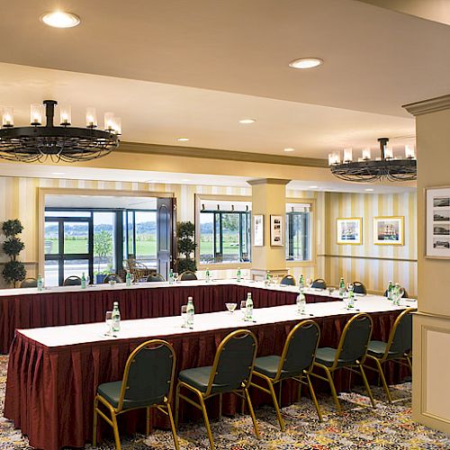 A conference room with a U-shaped table setup, chairs arranged around it, bottled water placed on the tables, and large windows offering an outside view.