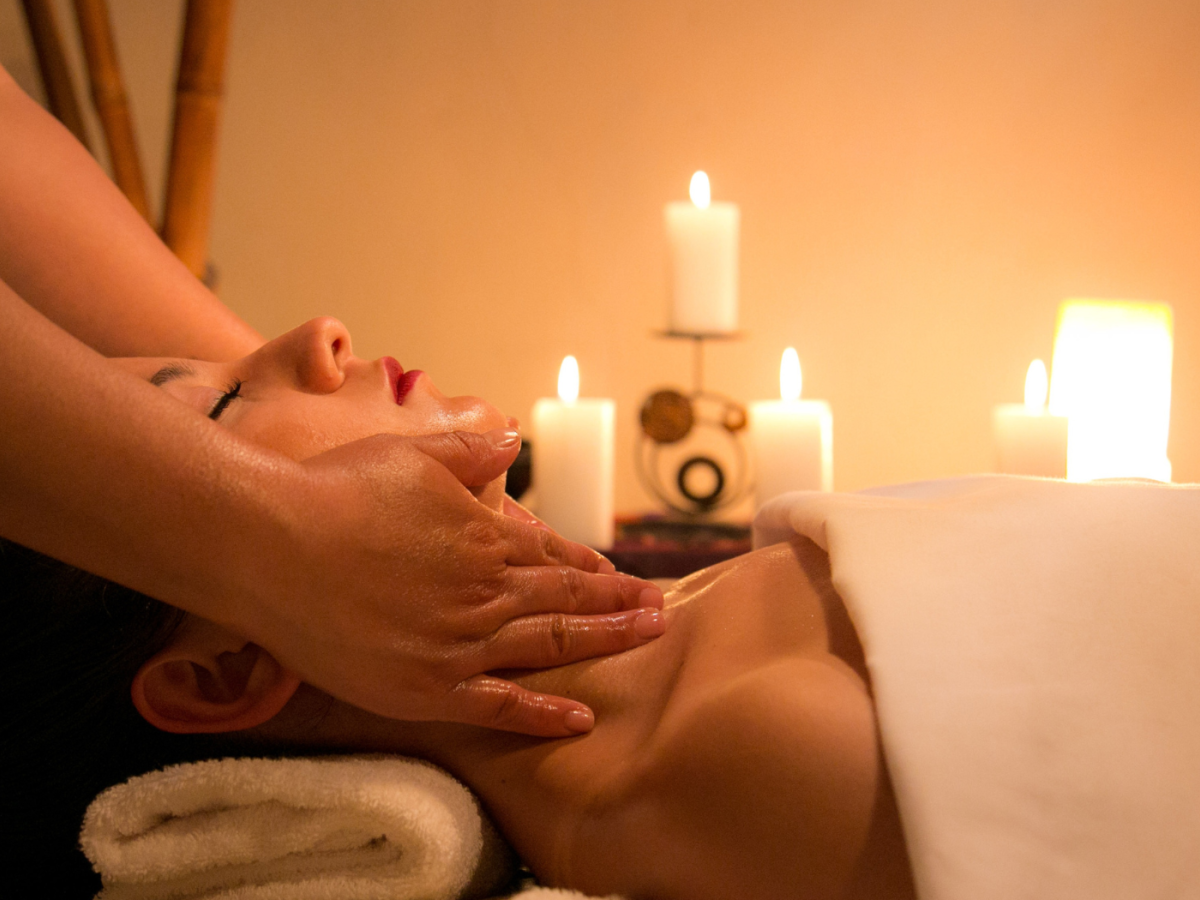 A person is receiving a facial massage in a serene setting with lit candles in the background, creating a calming and relaxing atmosphere.