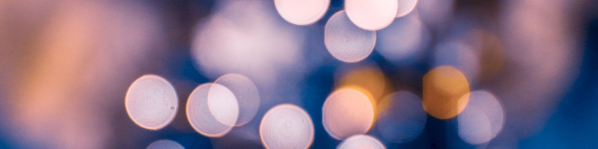 An out-of-focus image of a Christmas tree adorned with lights, creating a bokeh effect with circular light spots in various colors.