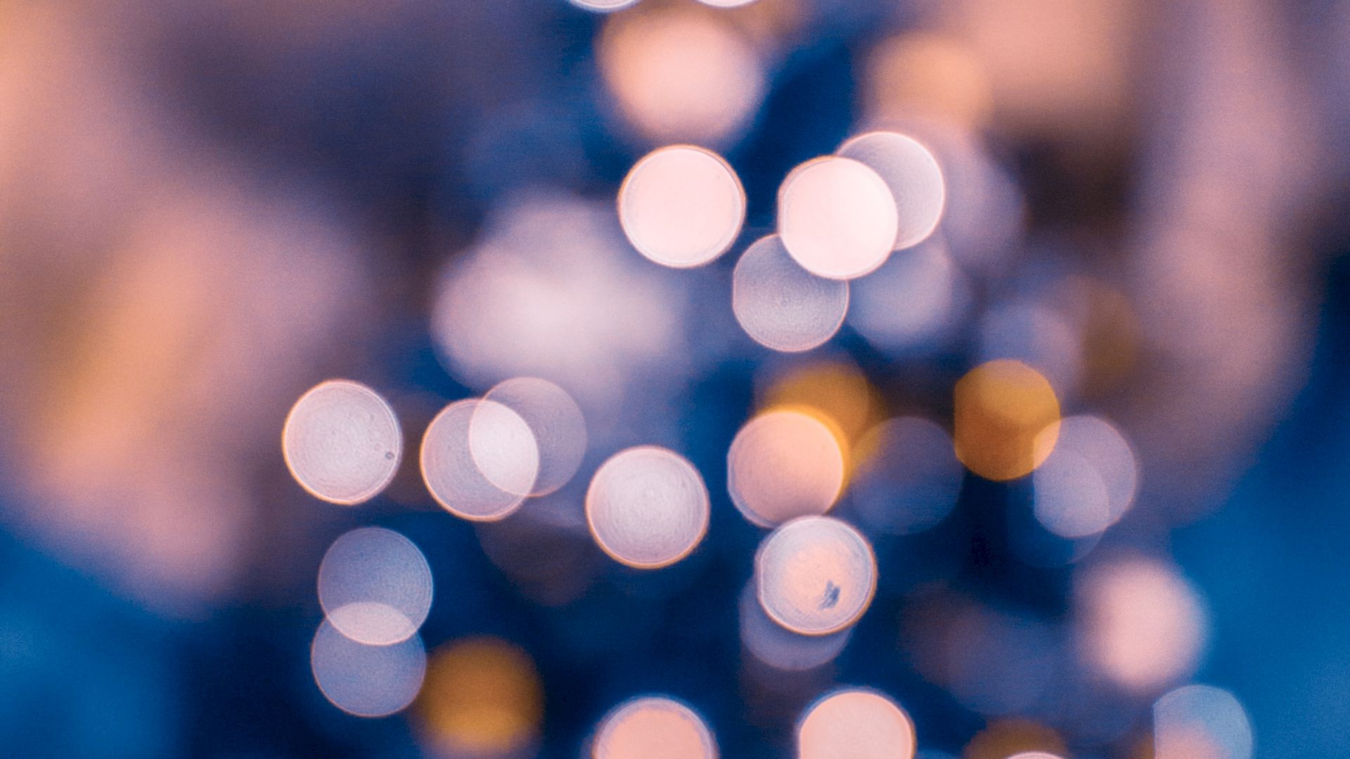 An out-of-focus image of a Christmas tree adorned with lights, creating a bokeh effect with circular light spots in various colors.
