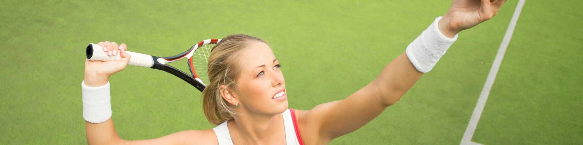 A woman in athletic wear is preparing to serve a tennis ball on a green court, holding a racket in one hand and a ball in the other hand.