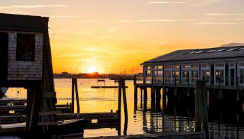 A serene sunset over a waterfront with wooden docks and buildings, casting reflections on the calm water ending the sentence.