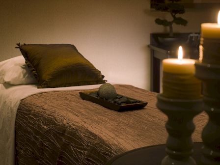 A cozy, dimly lit room with a made bed, a pillow, burning candles, and a decorative tray with a ball, creating a relaxing atmosphere.