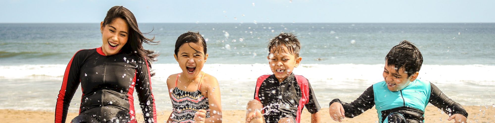 Four children are sitting by the pool, splashing water, and enjoying a sunny day at the beach with cheerful expressions.