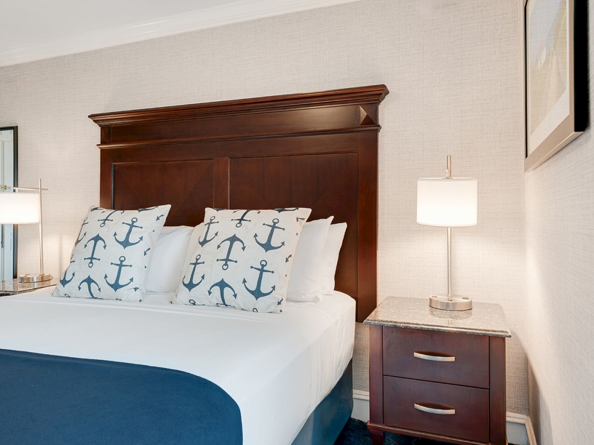 A neatly made bed with anchor-themed pillows, a wooden headboard, two bedside tables with lamps, and framed artwork on the wall.