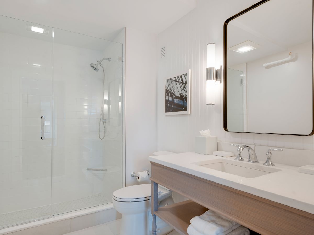 This image shows a modern bathroom with a glass shower, toilet, large mirror, sink, and countertop. Towels are neatly folded below the counter.