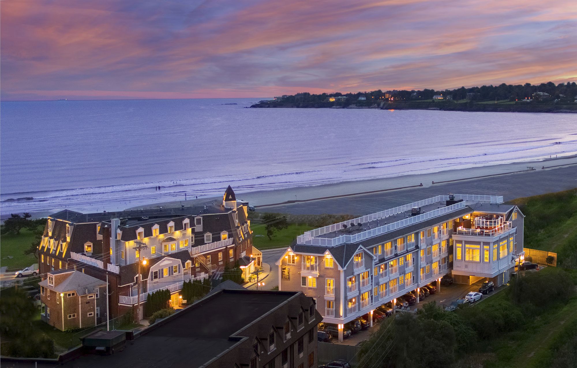 The image shows a coastal resort at dusk with lit buildings, a sandy beach, and a colorful sky.