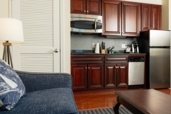 The image shows a kitchenette with wooden cabinets, a microwave, refrigerator, dishwasher, couch, table, and a lamp in the living space, ending the sentence.