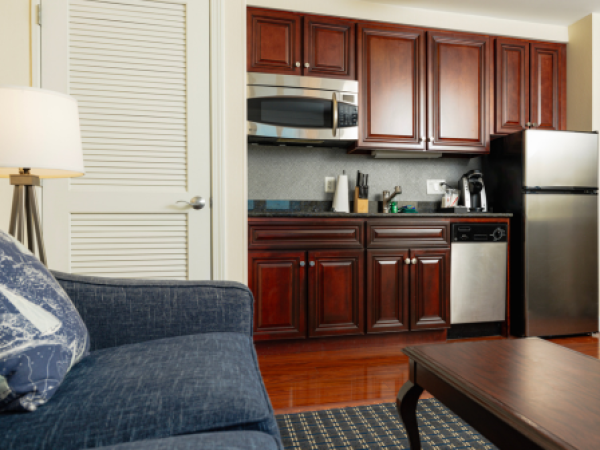 The image shows a kitchenette with wooden cabinets, a microwave, refrigerator, dishwasher, couch, table, and a lamp in the living space, ending the sentence.