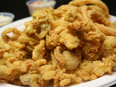 The image shows a plate of fried seafood, including clams and onion rings, with dipping sauces in small containers in the background.