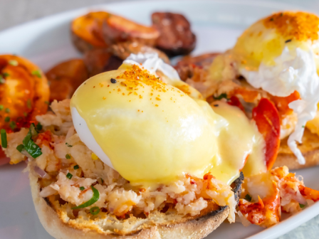 A plate of eggs benedict with poached eggs, hollandaise sauce, toasted English muffins, roasted tomatoes, and potatoes.