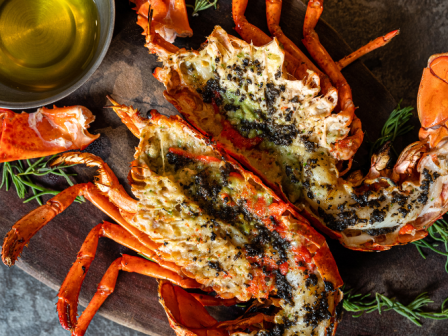 The image features a grilled lobster dish served on a wooden platter, accompanied by a bowl of melted butter and garnished with herbs.