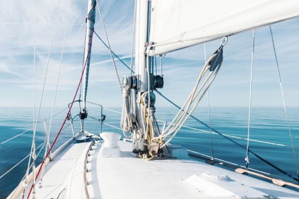 A view from the deck of a sailboat on calm waters with the sails partially up under a clear sky, creating a serene and tranquil scene.