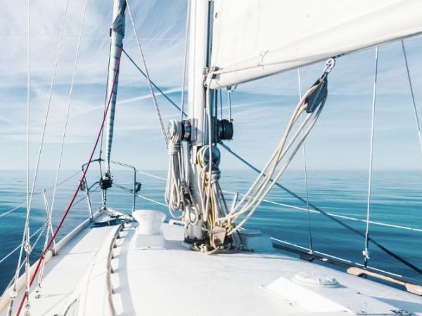 A view from the deck of a sailboat on calm waters with the sails partially up under a clear sky, creating a serene and tranquil scene.