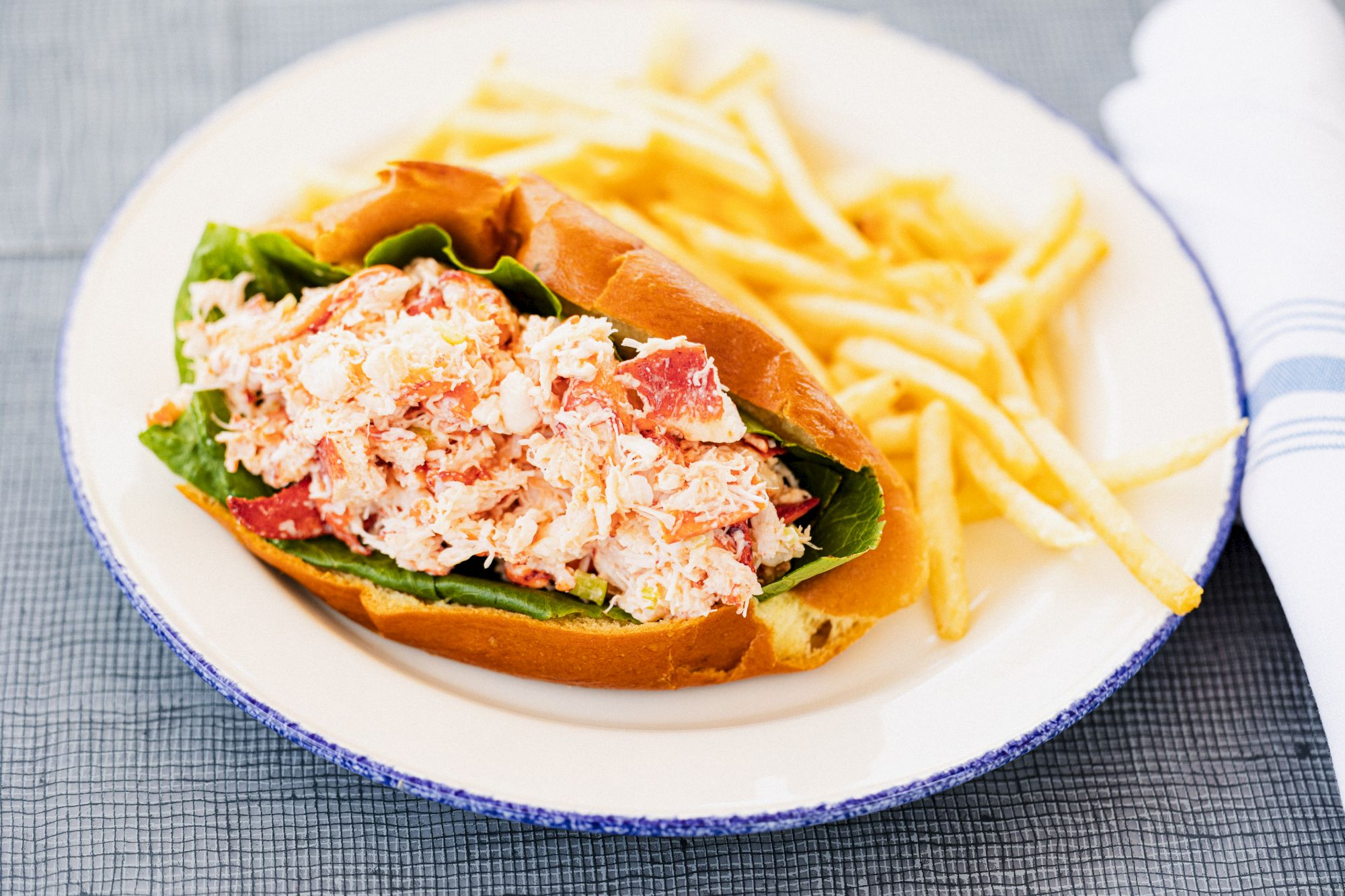 A lobster roll with lettuce on a plate served alongside a side of French fries.