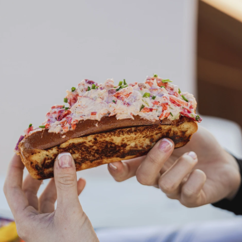 The image shows a person holding a lobster roll filled with lobster salad in a toasted bun.