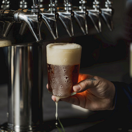 A person is pouring a glass of beer from a tap, with several other beer taps visible in the background.