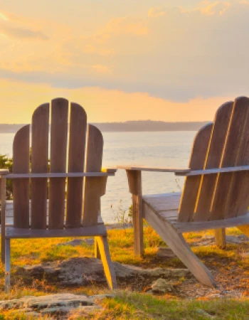 Two wooden chairs overlook a serene body of water during a beautiful sunset, creating a peaceful and inviting setting.