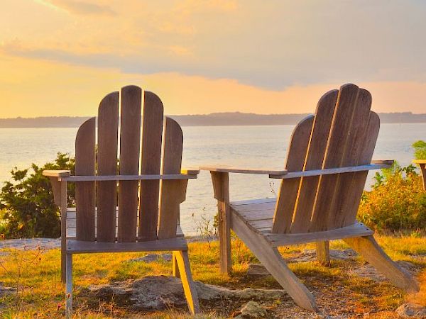 Two wooden chairs overlook a serene body of water during sunset, providing a peaceful, scenic spot for relaxation by the shore.
