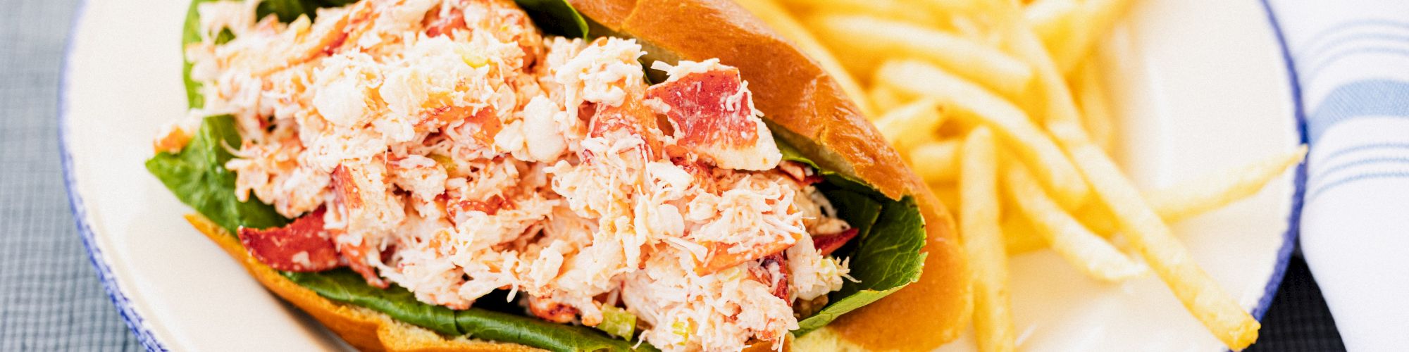 A lobster roll with lettuce on a plate served alongside a side of French fries.