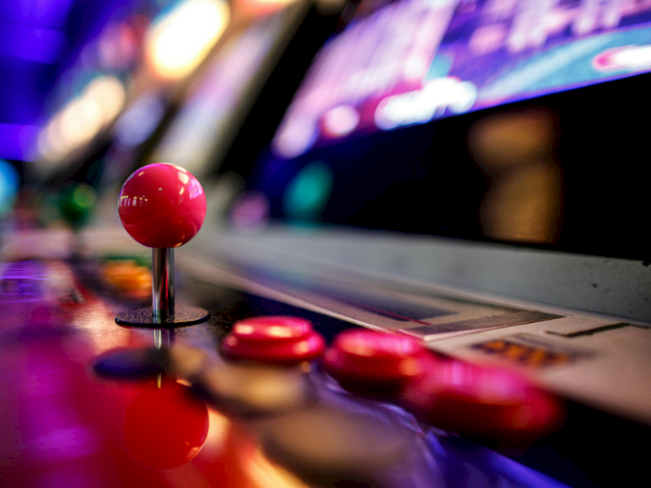 A red joystick on an arcade machine, with glossy buttons and a blurred neon-lit background, classic retro gaming vibe.