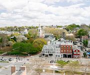 Aerial view of a small town with tree-lined streets, church steeples, and rooftops under a cloudy sky.