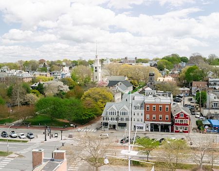 Aerial view of a small town with tree-lined streets, church steeples, and rooftops under a cloudy sky.