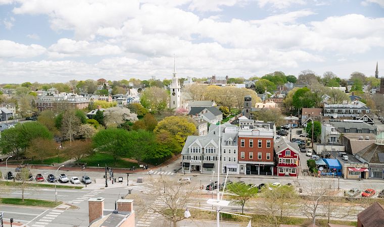 Aerial view of a small town with tree-lined streets, church steeples, and rooftops under a cloudy sky.