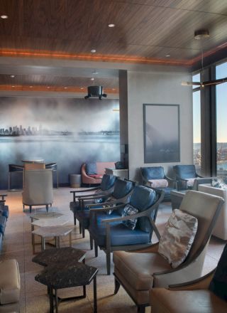 A modern lounge with cushioned chairs and tables features large windows with a view of a waterfront and ferris wheel, also wall art.