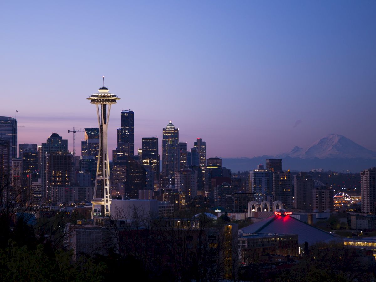 The image shows the nighttime skyline of Seattle, featuring the Space Needle, downtown skyscrapers, and Mount Rainier in the distance.