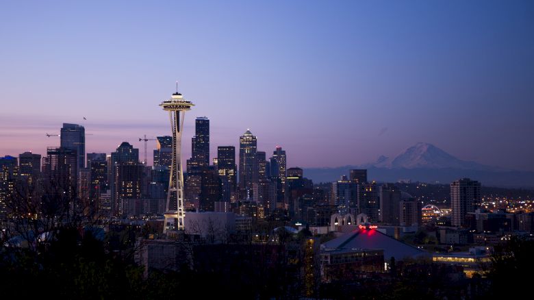 The image shows the nighttime skyline of Seattle, featuring the Space Needle, downtown skyscrapers, and Mount Rainier in the distance.